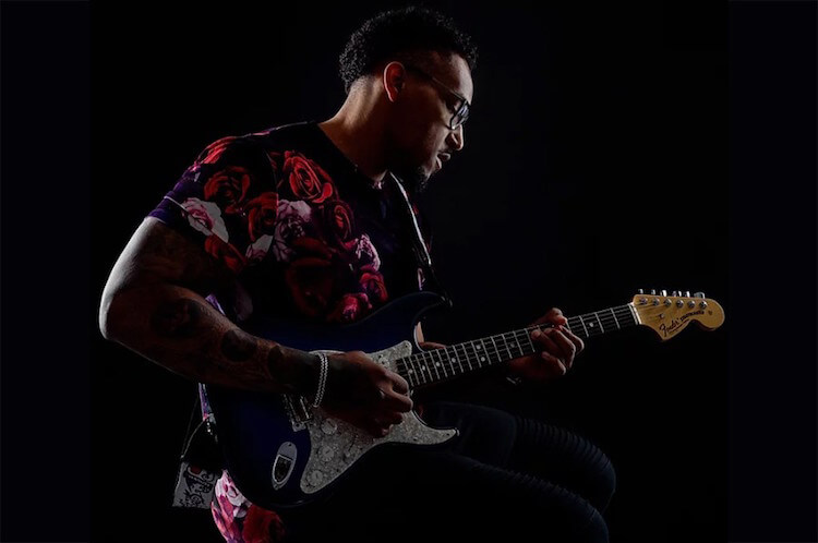 Joe Barksdale Black Man wearing glasses and a red shirt playing a white guitar Song of the Day | Eat Sleep Breathe Music